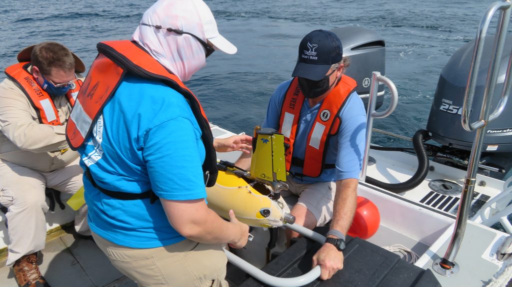 Three members of the field team on a boat preparing to deploy the yellow glider named Franklin.