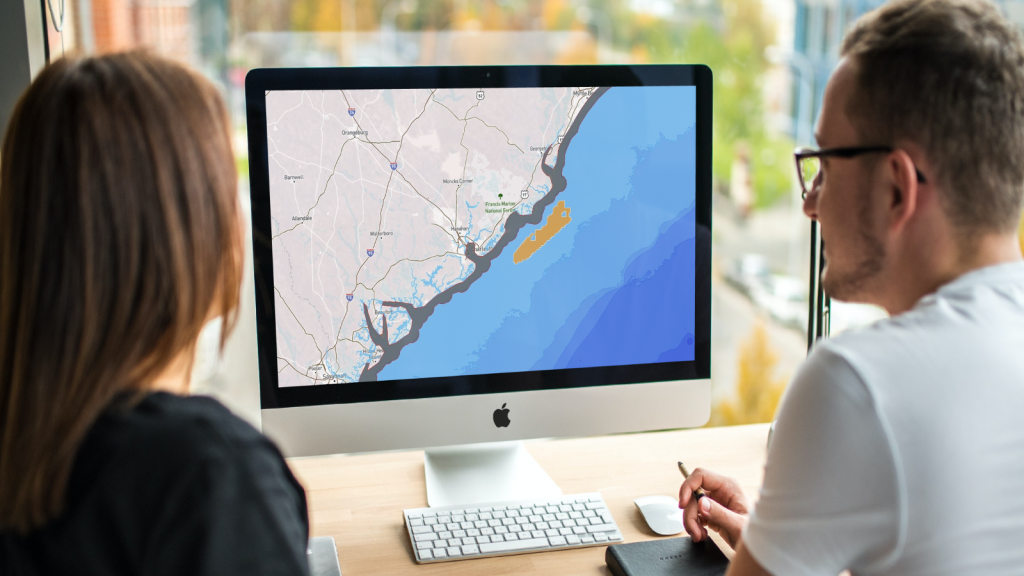 Two people are looking at a computer screen which shows a map of the coast of South Carolina with an orange designated area in the ocean.